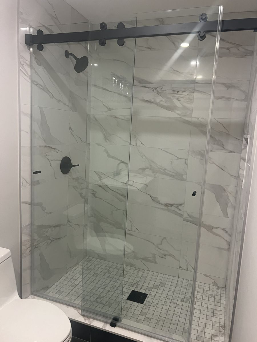 Marble-look tile shower with matte black sliding glass door, black fixtures and square drain