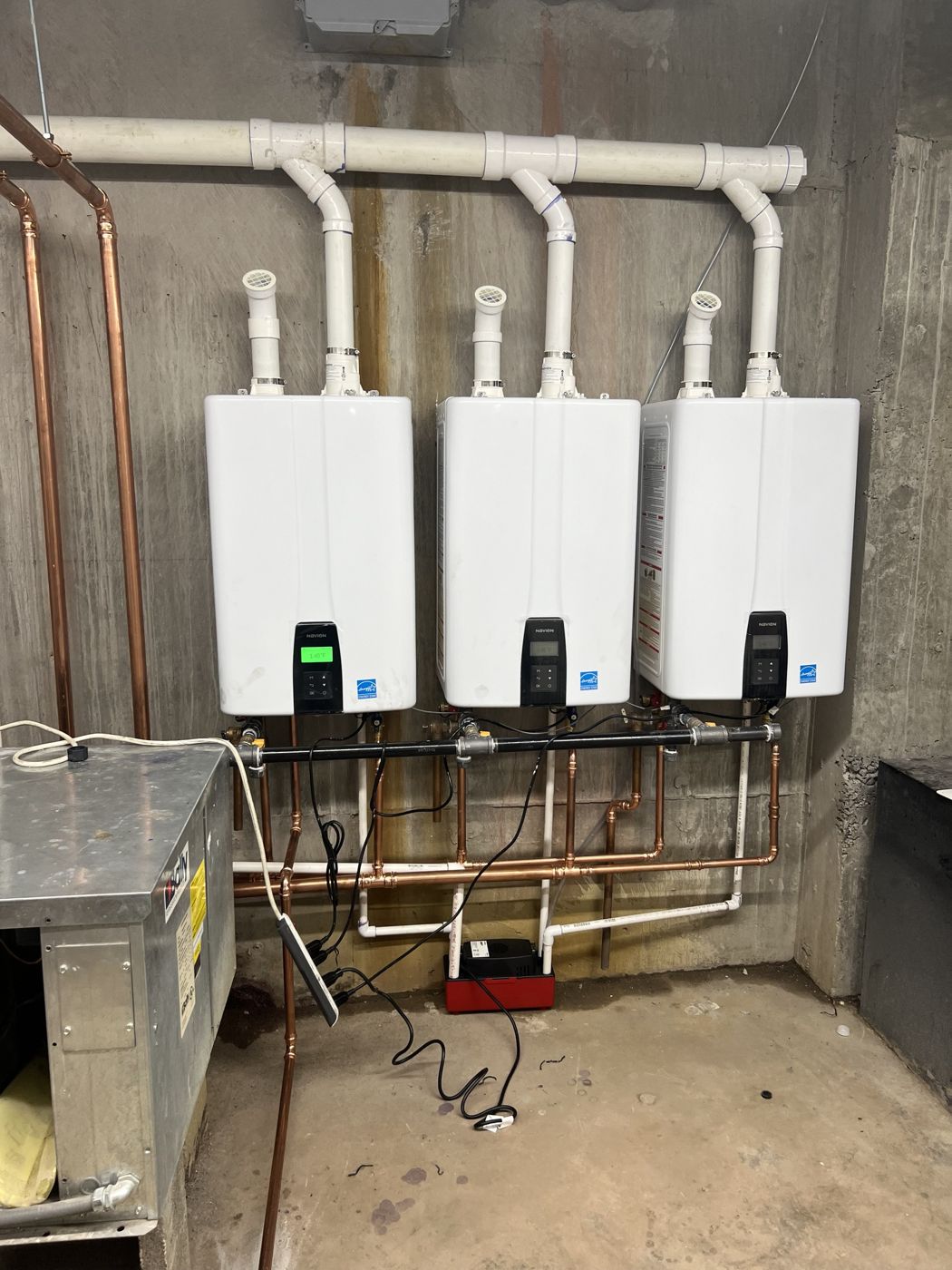 Three Navien tankless water heaters installed side by side at a hotel